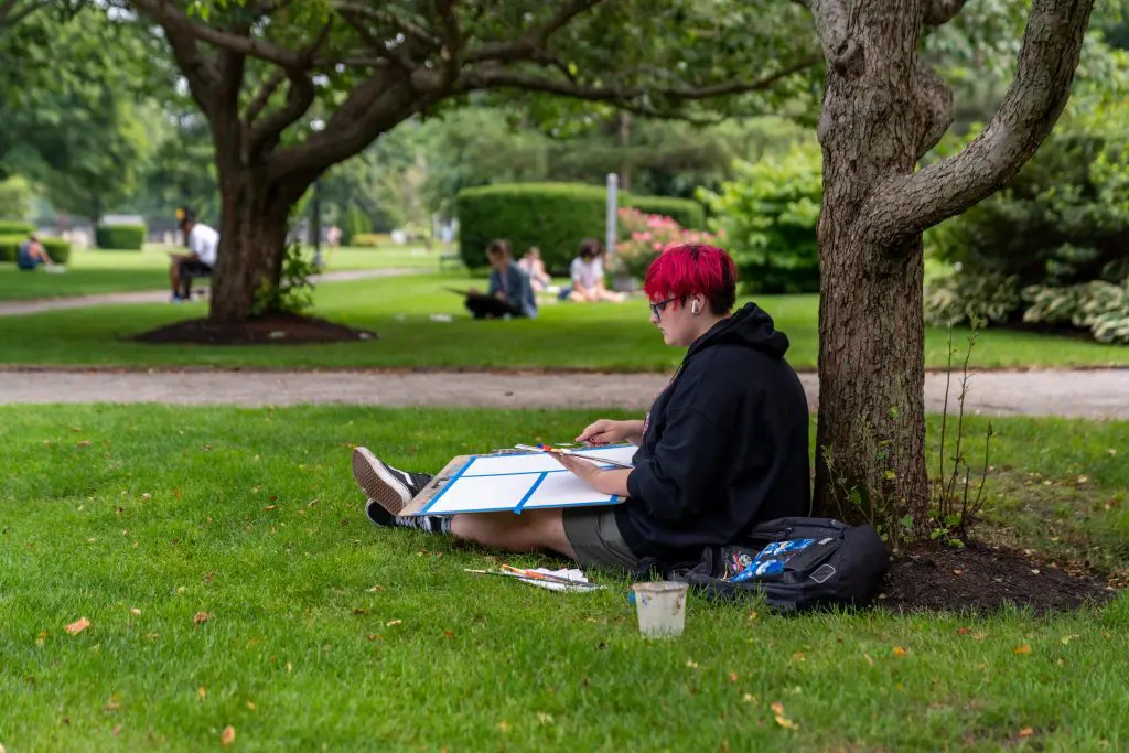 A person sitting next to a tree with painting supplies
