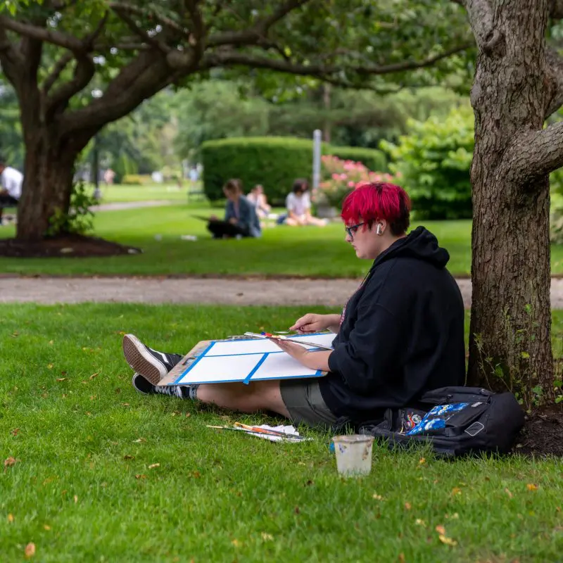 A person sitting next to a tree with painting supplies