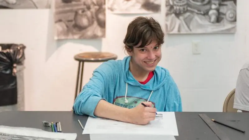 A person drawing something with charcoal still-life drawing behind them