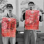 Two people holding typographic prints. The picture is grayscale except for the type on the prints